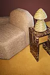 En beige, skulpterad soffa bredvid ett marmormönstrat sidobord med en dekorativ bordslampa.