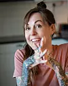 Kvinna med tatueringar i rosa topp ler inomhus.