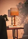 Bordslampa på sidobord med böcker och kopp i varmt ljus mot skuggad vägg.