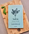 En ljusblå bok med texten Salvia ligger på en träskärbräda med några gröna salviablad.