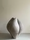 En grå keramisk skulptur står på ett bord framför en ljus vägg.