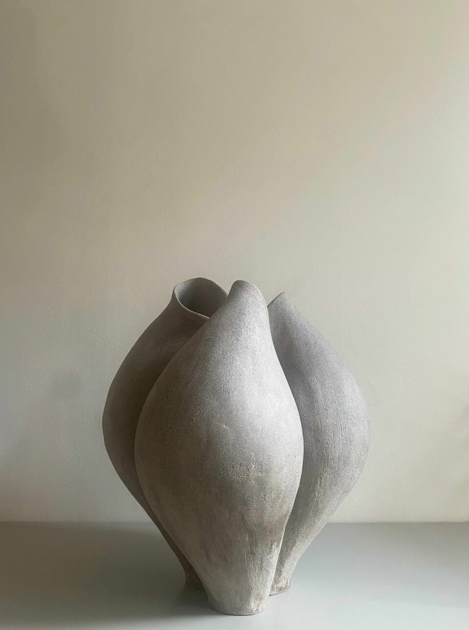 En grå keramisk skulptur står på ett bord framför en ljus vägg.