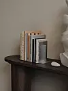 Flera böcker står på ett mörkt bord bredvid en vit dekorsten och en ljus skulptur mot en beige vägg.