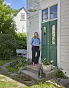 Kvinna står på en liten stenlagd farstukvist framför en grön dörr vid ett vitt hus.
