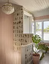 Ljust trapphus med blommig tapet, kristallkrona, spegel och stor krukväxt.