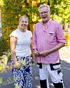 Två personer står utomhus i ett grönskande område i varmt ljus.