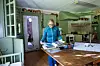 Kvinna i blå kläder bläddrar i tidningar vid ett träbord i ett kök.