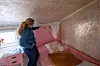 Person standing beside a pink bed and pointing toward the wall in a small bedroom.