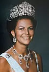 Porträtt av en kvinna med tiara, örhängen och halsband med stora smycken mot mörk bakgrund.