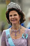 Kvinna i lila klänning med tiara, halsband, örhängen och ljusblå sash.