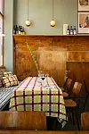 Restauranghörna med rutiga dukar, träpanel, flaskor på hyllan och två vägglampor.