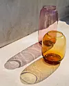 Två färgade glas i rosa och bärnstensfärgat står i solen på en ljus yta.