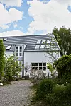 Vitt hus med solpaneler på taket, grusgång och frodig trädgård.
