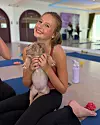 Leende flicka sitter på en yogamatta och håller en valp i ett ljust träningsrum.