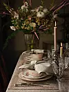 Dukat bord med porslin, glas, ljus och blomsterarrangemang i dämpat ljus.