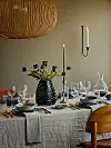 Väldukad matplats med ljus, glas, tallrikar, mörk vas med blommor och en stol i förgrunden.