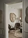 Vardagsrum med två rottingstolar, bord, golvlampa och en stor texturerad väggdekoration.
