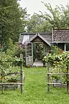 Liten trädgårdsentré med växthus, blomsterbäddar och trähus omgiven av grönska.