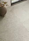 Ljust stenlagt golv bredvid ett fönster med en stor kruka och torra grenar.