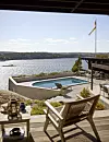 Terrass med möbler, pool och sjöutsikt under klar himmel.
