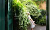 En person står bredvid en vägg med vitblommande jasmin i en trädgård.
