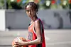Ung basketspelare i röd tröja håller en basketboll på en utomhusplan.