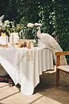 Vit påfågel vid ett vitt dukat bord med blommor och ljus framför en grön växtvägg.