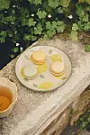 Tre macarons på en mönstrad tallrik på en stenbänk med grön växtlighet i bakgrunden.