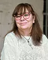 Kvinna med röda glasögon och vit tröja mot ljus bakgrund.