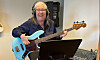 En kvinna med hörlurar spelar elbas vid ett notställ i en musikstudio.
