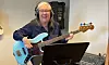 En kvinna med hörlurar spelar elbas vid ett notställ i en musikstudio.
