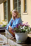 En kvinna i blå skjorta sitter på trappan utanför ett hus bredvid en kruka med blommor.