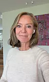 Kvinne tar en selfie innendørs med et fargerikt bilde på veggen bak seg.