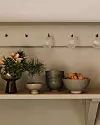 Hyllplan med blomsterarrangemang, keramiska skålar och en skål med små bakverk under tre vägglampor.