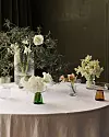 Rundt bord med vita blommor i olika vaser och krukor i ett dämpat inomhusljus.