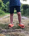 Barns ben i shorts och orange djurskor på en grusväg med ett plåster på ena benet.