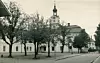 Svartvit bild av ett rådhus bakom träd längs en öppen gata eller torg.