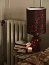 Bordslampa med mörkröd skärm, böcker och ett tänt ljus bredvid en radiator.
