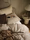 Randig säng med kuddar, filt och en lampa i ett sovrum.
