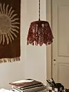 Vinröd lampskärm i spets framför ljus vägg med inredningsdetaljer.