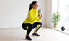 Kvinna i gul jacka gör knäböj med kettlebell i ett ljust rum.