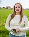 Kvinna i ljus tröja står på ett grönt fält och håller en mobiltelefon.