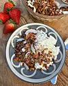 Tallrik med keso och granola på ett träbord bredvid färska jordgubbar.