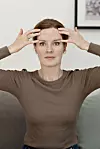 Kvinna sitter i soffa och gör ansiktsyoga med händerna mot pannan.
