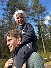 Barn sitter på skuldrene til en voksen på tur i skogen en solrik dag