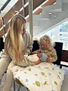 Barn holder nyfødt baby på sykehusets venterom sammen med en voksen.