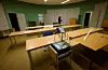 Tomt mötesrum med bord, stolar, projektor och gröna väggar i en bunkerliknande lokal.