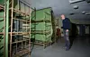 En man står i ett källarliknande rum med metallsängar, gröna väggar och taklampor.