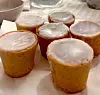 6 glaserade mazarinen står på ett papper på ett dukat bord.