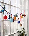 Juldekorationer i olika färger hänger framför ett fönster med stjärnljus.